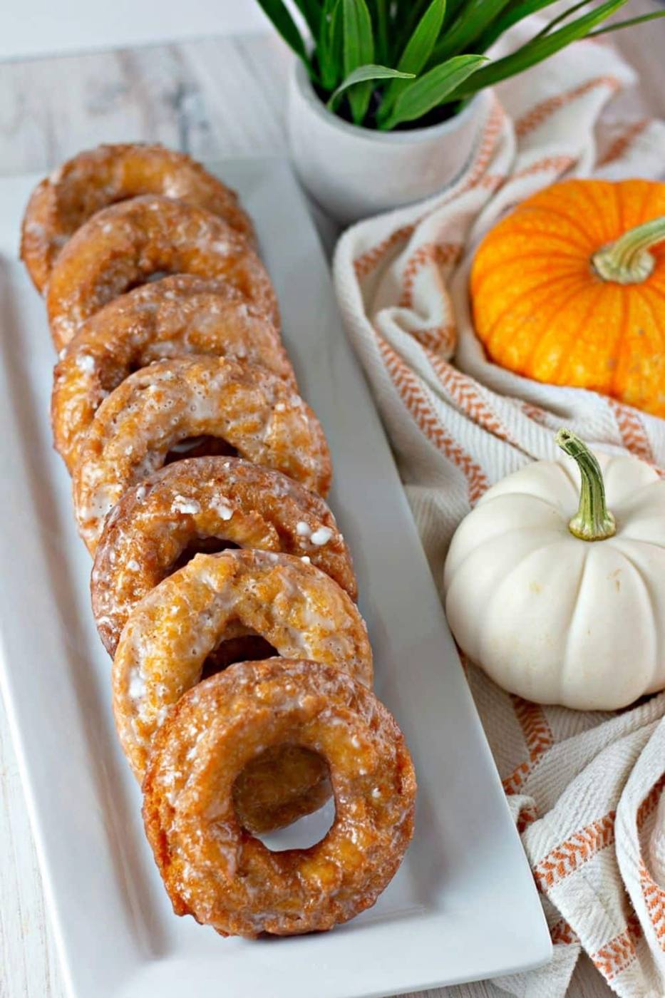 Stack of glazed pumpkin donuts on a white plate