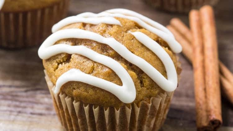 Close-up of a pumpkin muffin with cream cheese glaze beside cinnamon sticks