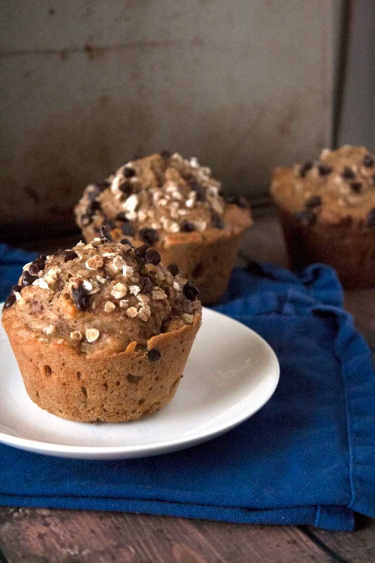 Pumpkin oatmeal chocolate chip muffin on a white plate with more muffins behind it on a blue napkin
