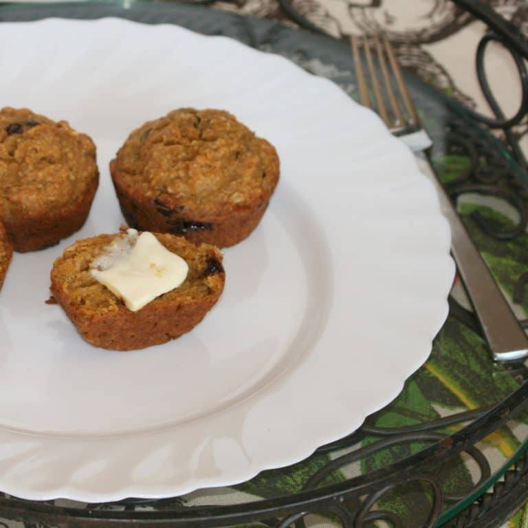 Pumpkin chocolate chip muffins on a white plate, one split open with a pat of butter