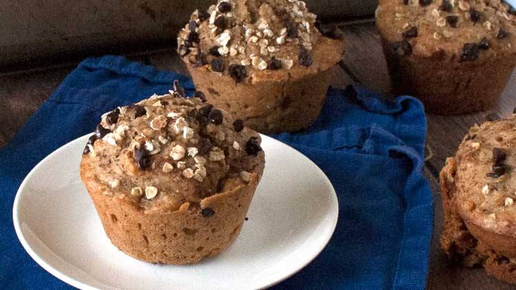 Pumpkin chocolate chip muffins with oat topping on a white plate and blue napkin