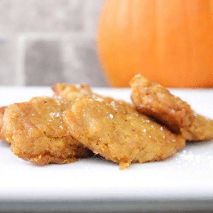 Golden homemade pumpkin patties dusted with powdered sugar on a white plate with a pumpkin in the background