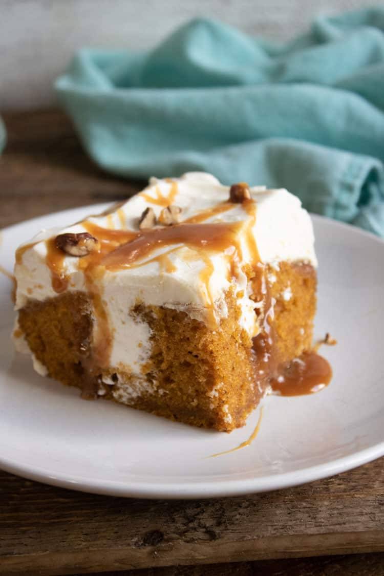 Slice of pumpkin poke cake with cream cheese topping, caramel drizzle, and pecans on a white plate