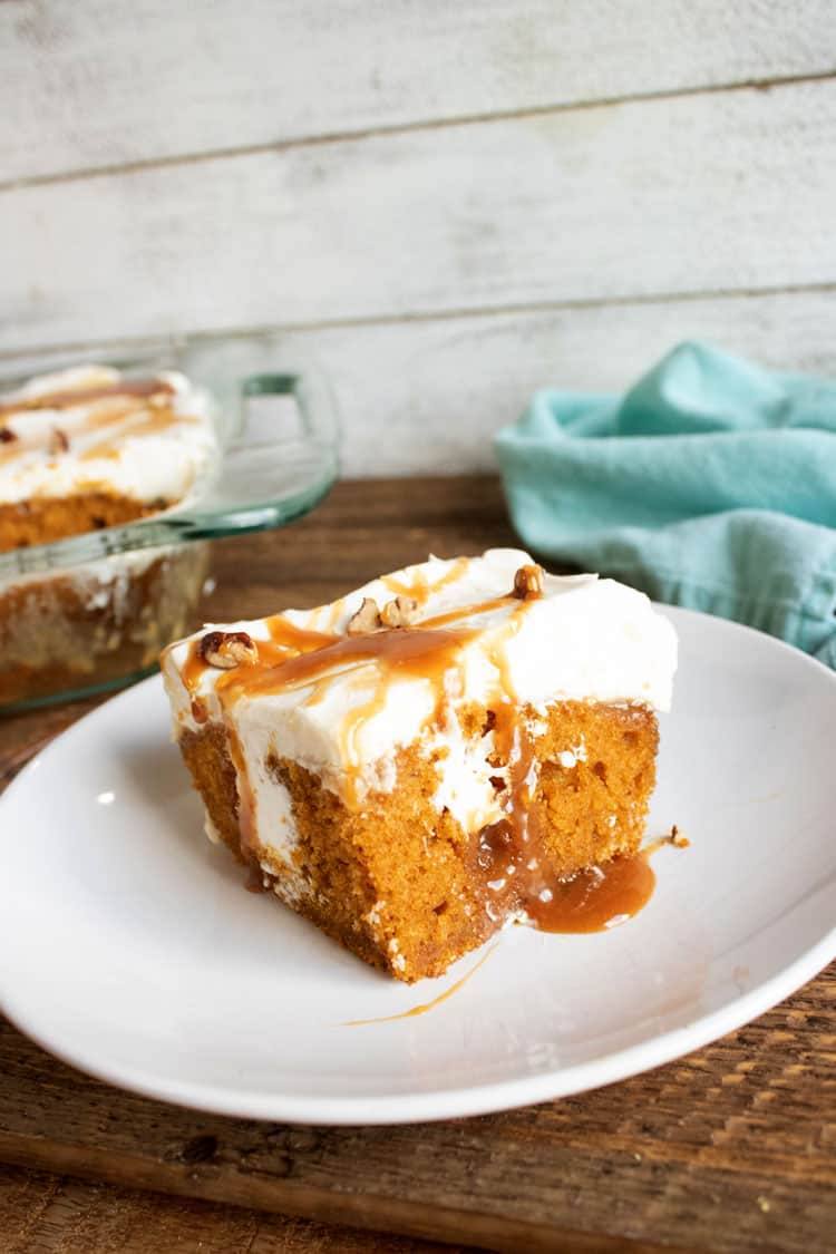 Slice of caramel pumpkin poke cake on a plate with the rest of the cake in a glass baking dish behind it