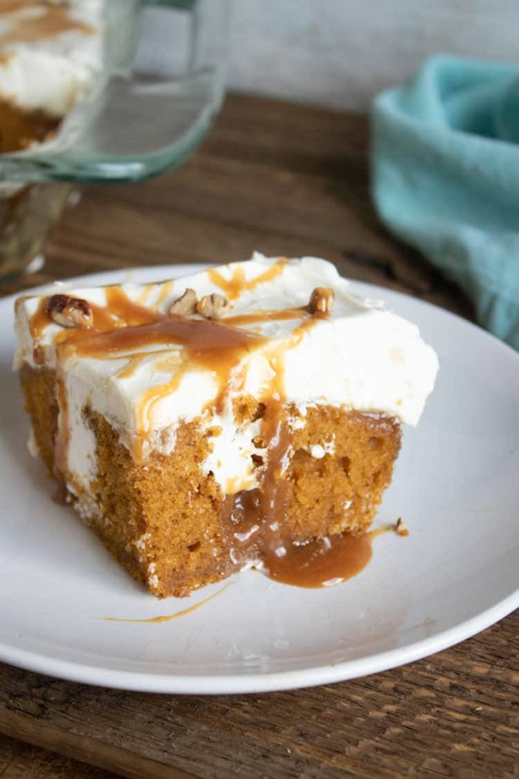 Close-up of a pumpkin poke cake slice showing caramel soaked into the holes, with a blue towel in the background