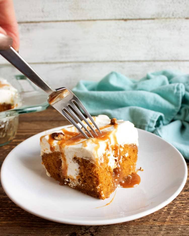 Fork cutting into a slice of pumpkin poke cake topped with caramel and pecans