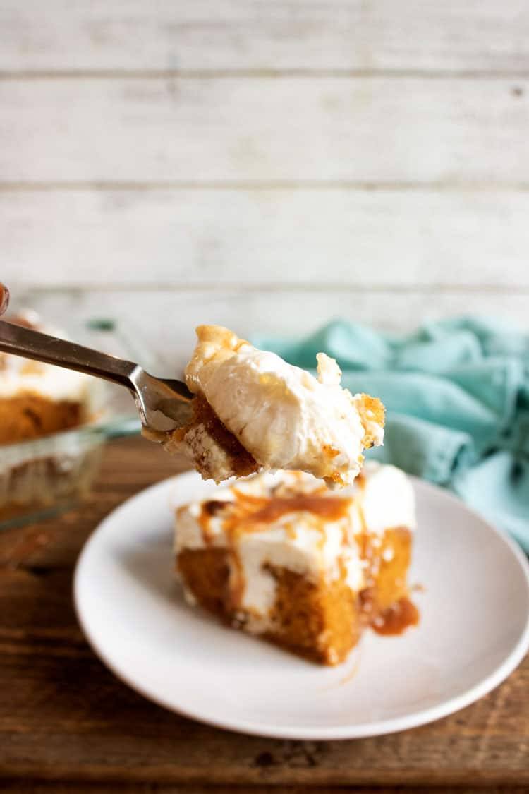 Spoonful of pumpkin poke cake held above a slice on a white plate