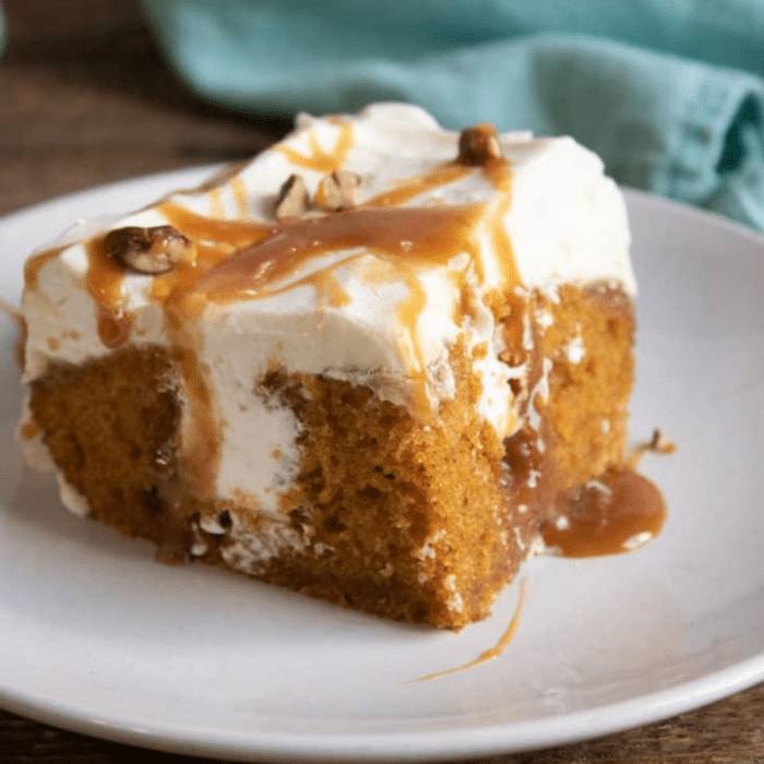 Slice of pumpkin poke cake with caramel drizzle, cream cheese topping, and pecans on a white plate
