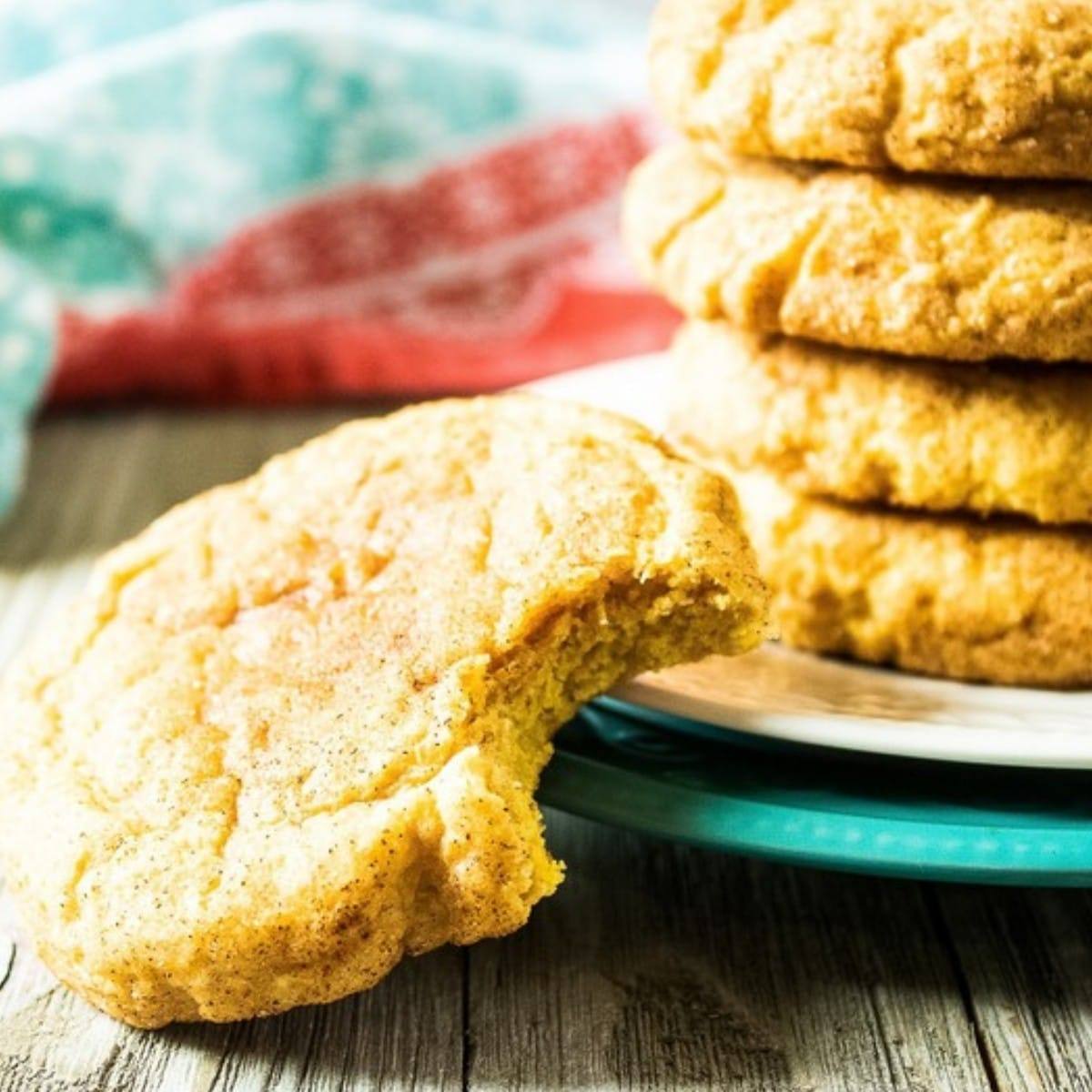 Pumpkin snickerdoodle with a bite taken out in front of a stack of cinnamon-sugar cookies