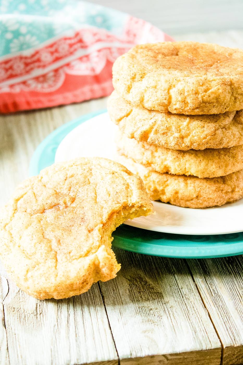 Stack of pumpkin snickerdoodle cookies with one bitten cookie in front on a teal plate