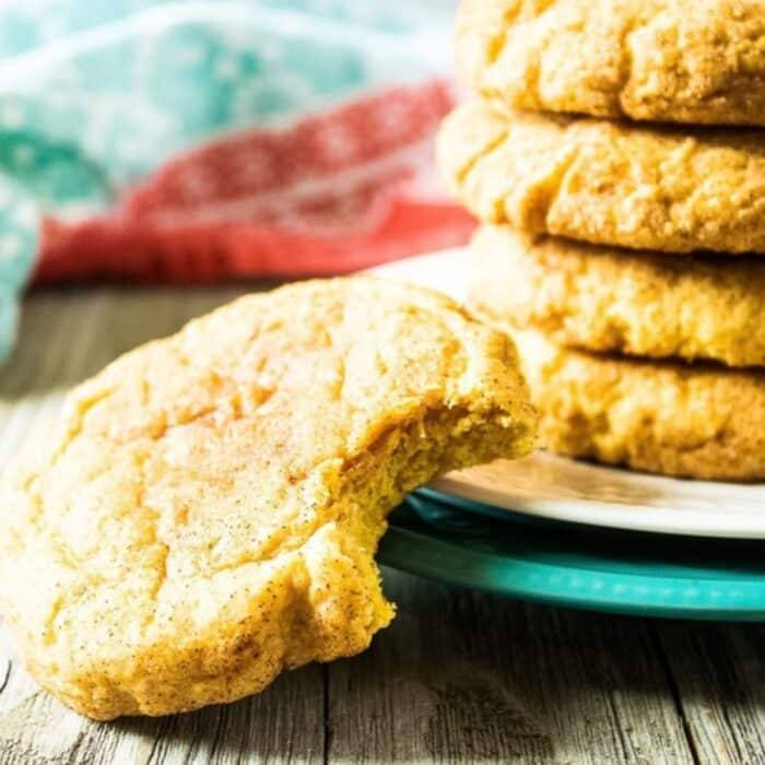Pumpkin snickerdoodle with a bite taken out in front of a stack of cinnamon-sugar cookies