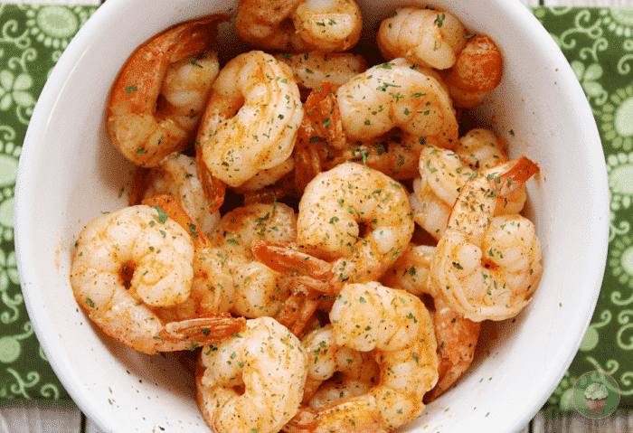 Overhead view of Cajun shrimp sprinkled with parsley in a white bowl on a green napkin