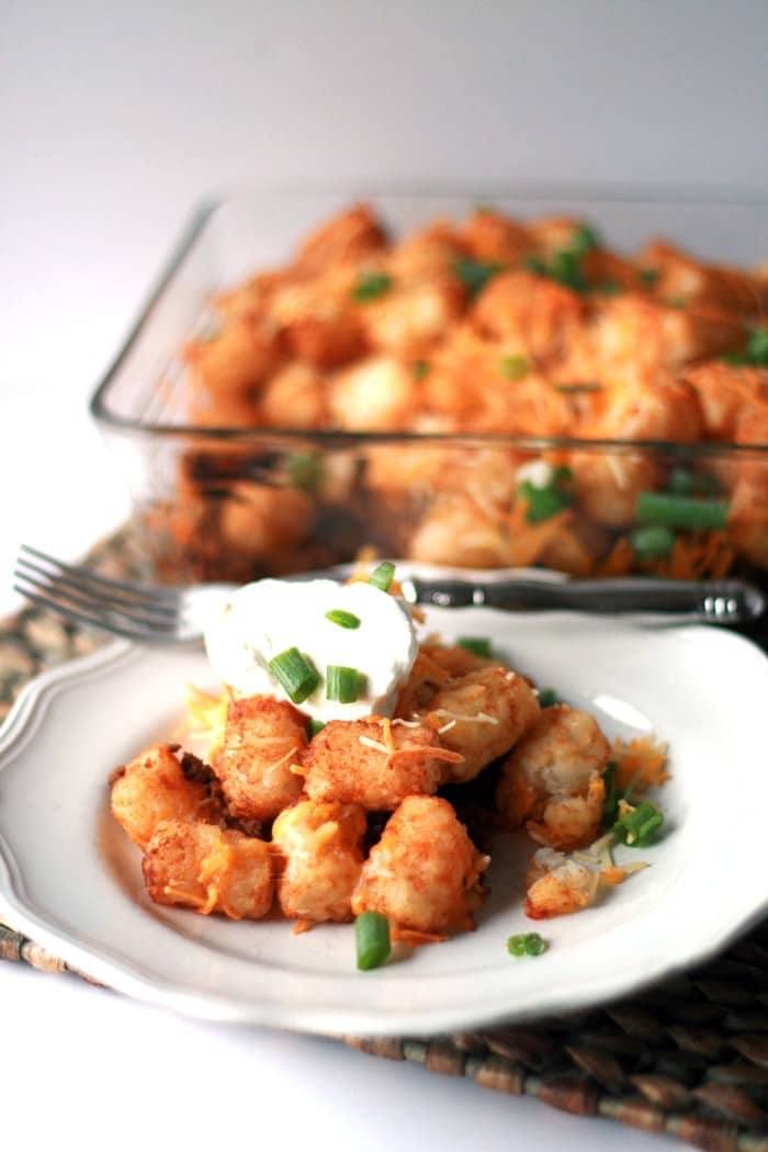 Serving of easy taco tater tot casserole with sour cream and sliced green onions