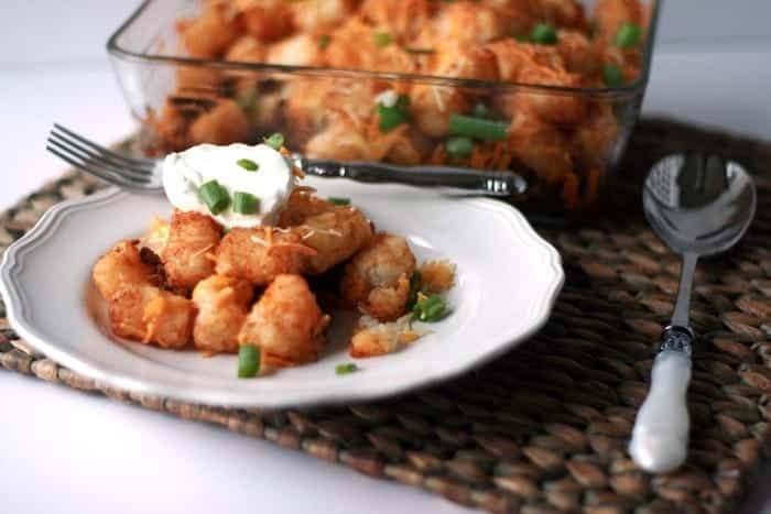 Plate of taco tater tot casserole topped with sour cream and green onions in front of the baking dish