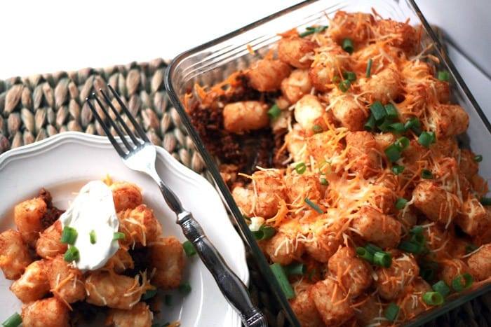 Overhead view of taco tater tot casserole in a glass baking dish next to a plated serving