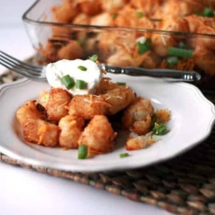 Easy taco tater tot casserole served on a white plate with sour cream and green onions