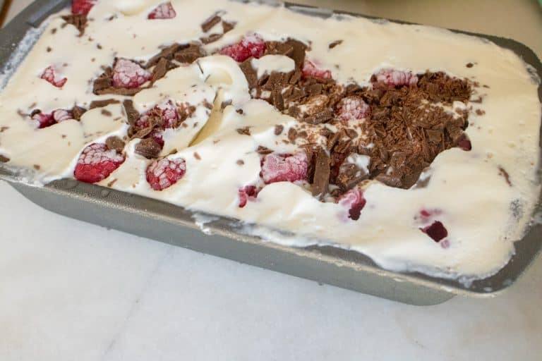silver loaf pan filled with all ingredients for Raspberry Chocolate Chunk No-Churn Ice Cream