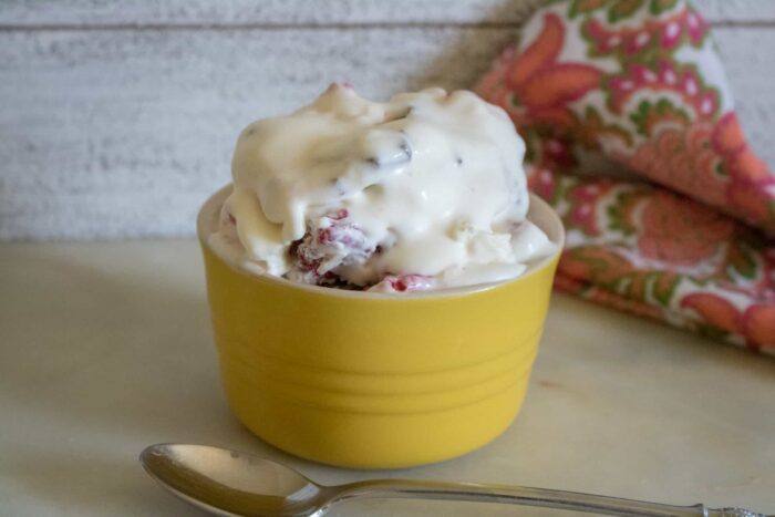 one scoop of Raspberry Chocolate Chunk No-Churn Ice Cream served in a yellow bowl with a silver spoon and a red print cloth napkin