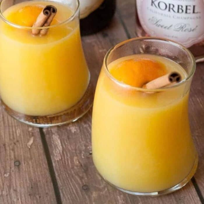 Two glasses of warm mulled mimosa cocktail garnished with cinnamon sticks and orange