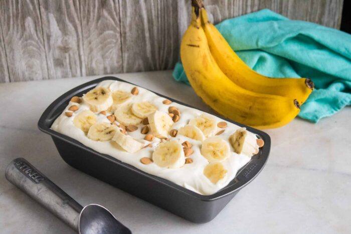 Reese's Peanut Butter Chips & Banana No-Churn Ice Cream ready to serve and next to a silver ice cream scoop, two bananas and a blue cloth napkin