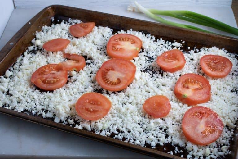 Cauliflower rice and sliced tomatoes spread on a baking sheet, ready to roast