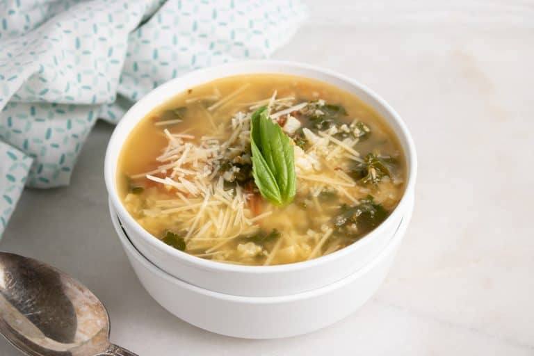 Bowl of roasted tomato and cauliflower rice soup with Parmesan and basil beside a teal patterned napkin