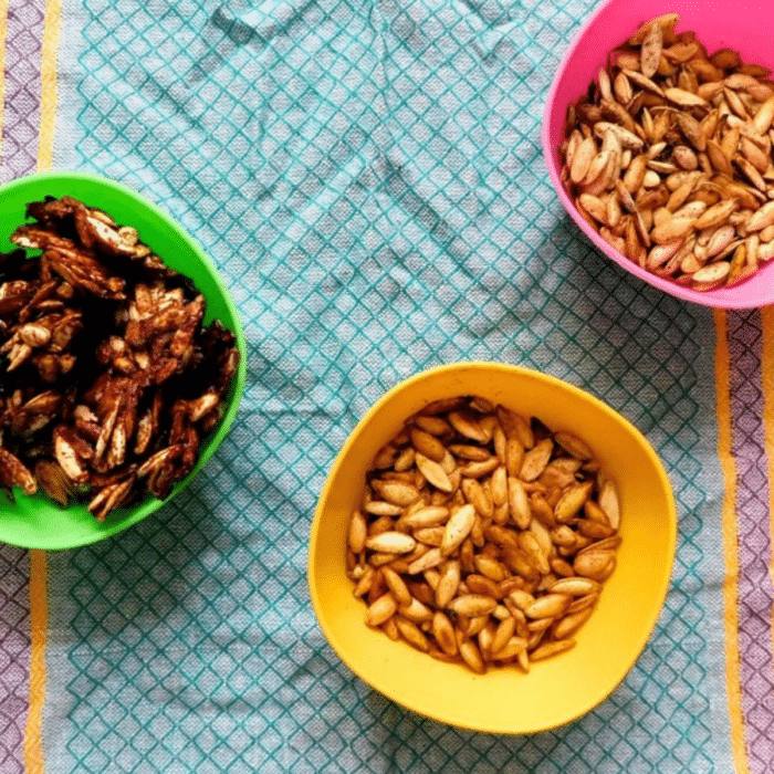 Three bowls of roasted pumpkin seeds in maple pumpkin spice, Indian-spiced, and dill vinegar flavors