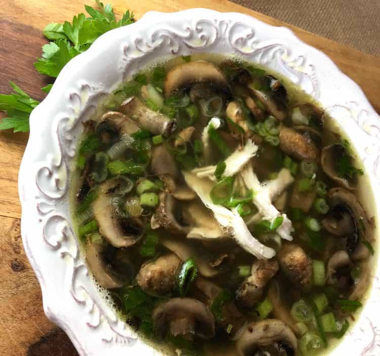 Overhead view of chicken marsala soup with browned mushrooms, rotisserie chicken and green onions in a white bowl