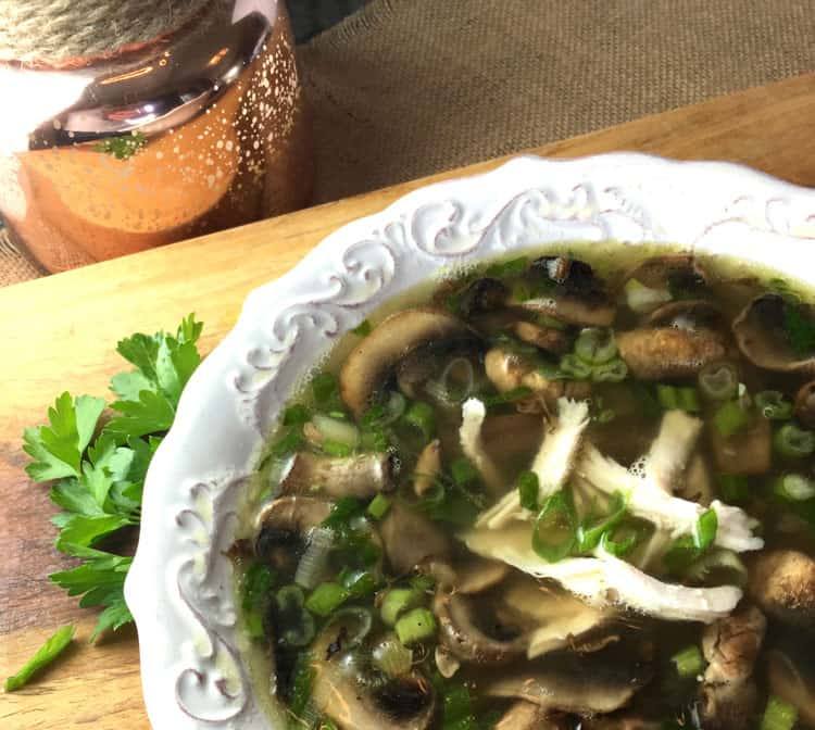 Bowl of easy chicken marsala soup with mushrooms and rotisserie chicken next to fresh parsley on a wooden board