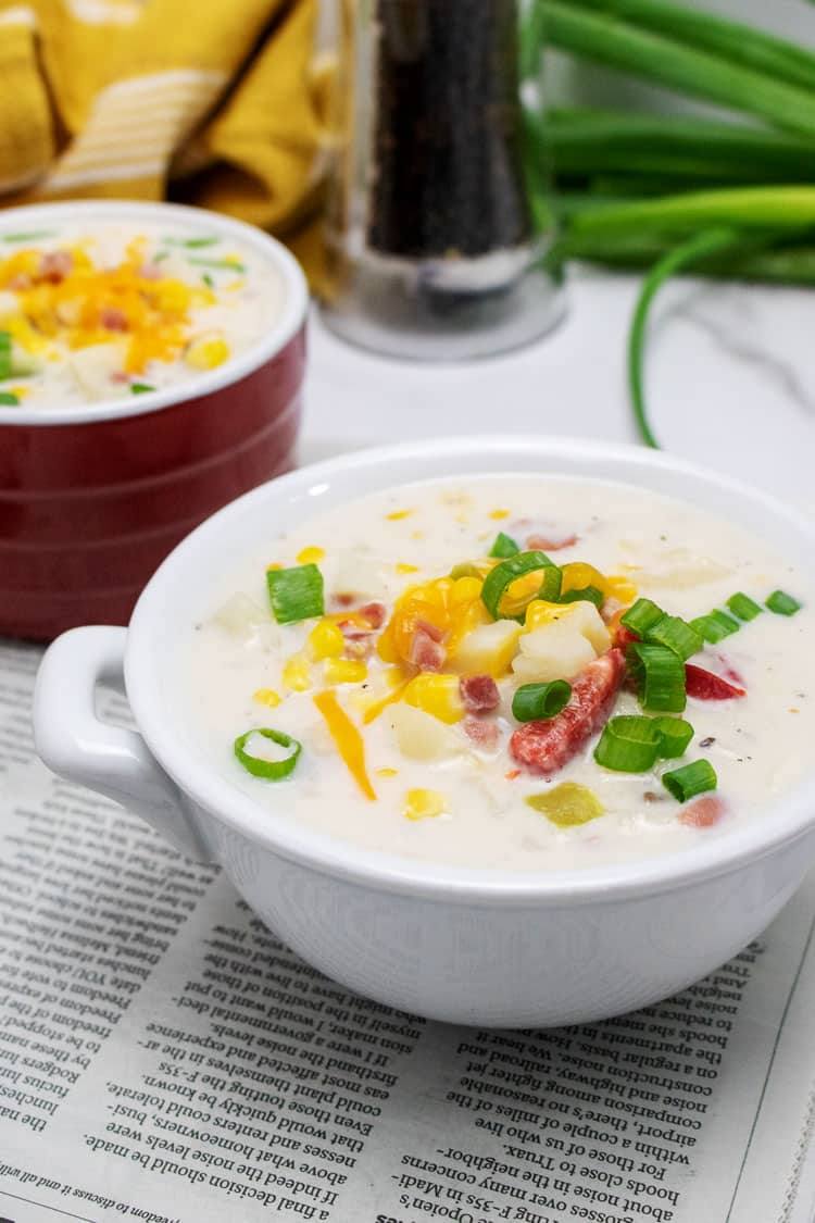 Slow cooker corn chowder with ham, potatoes and green onions in a white bowl