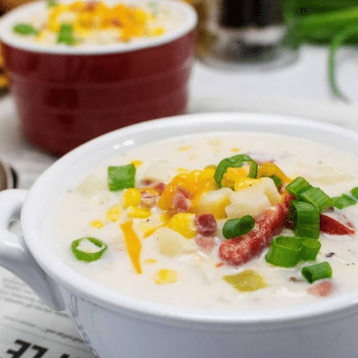 Slow cooker corn chowder with ham, potatoes and green onions in a white bowl