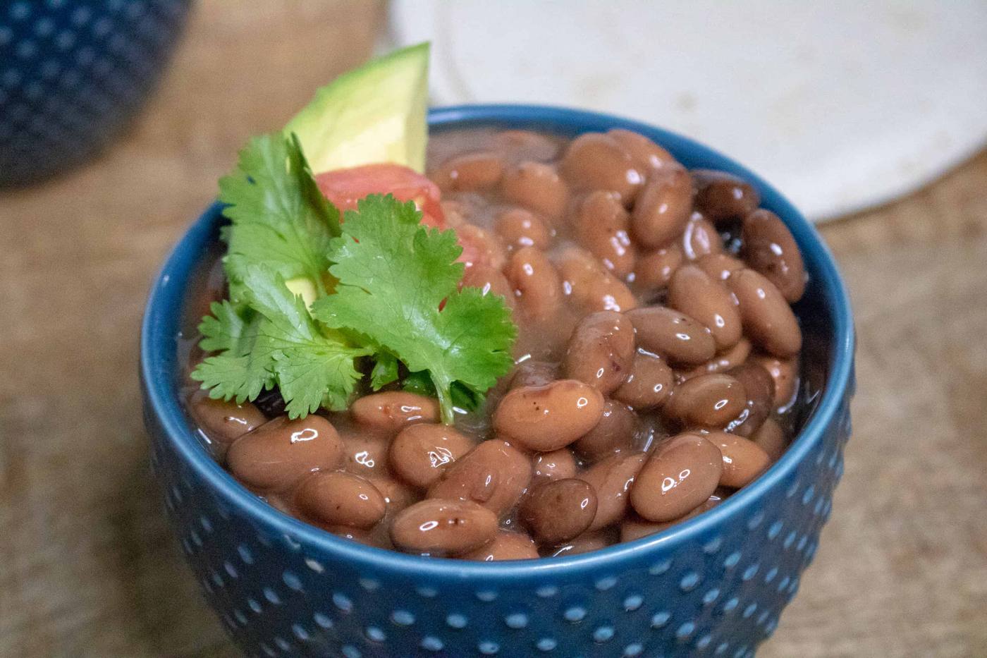 Complete Slow Cooker Pinto Beans in blue ceramic bowl with parsley garnish
