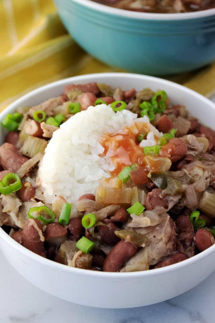 Crockpot red beans and rice in a white bowl with a scoop of white rice and scallions