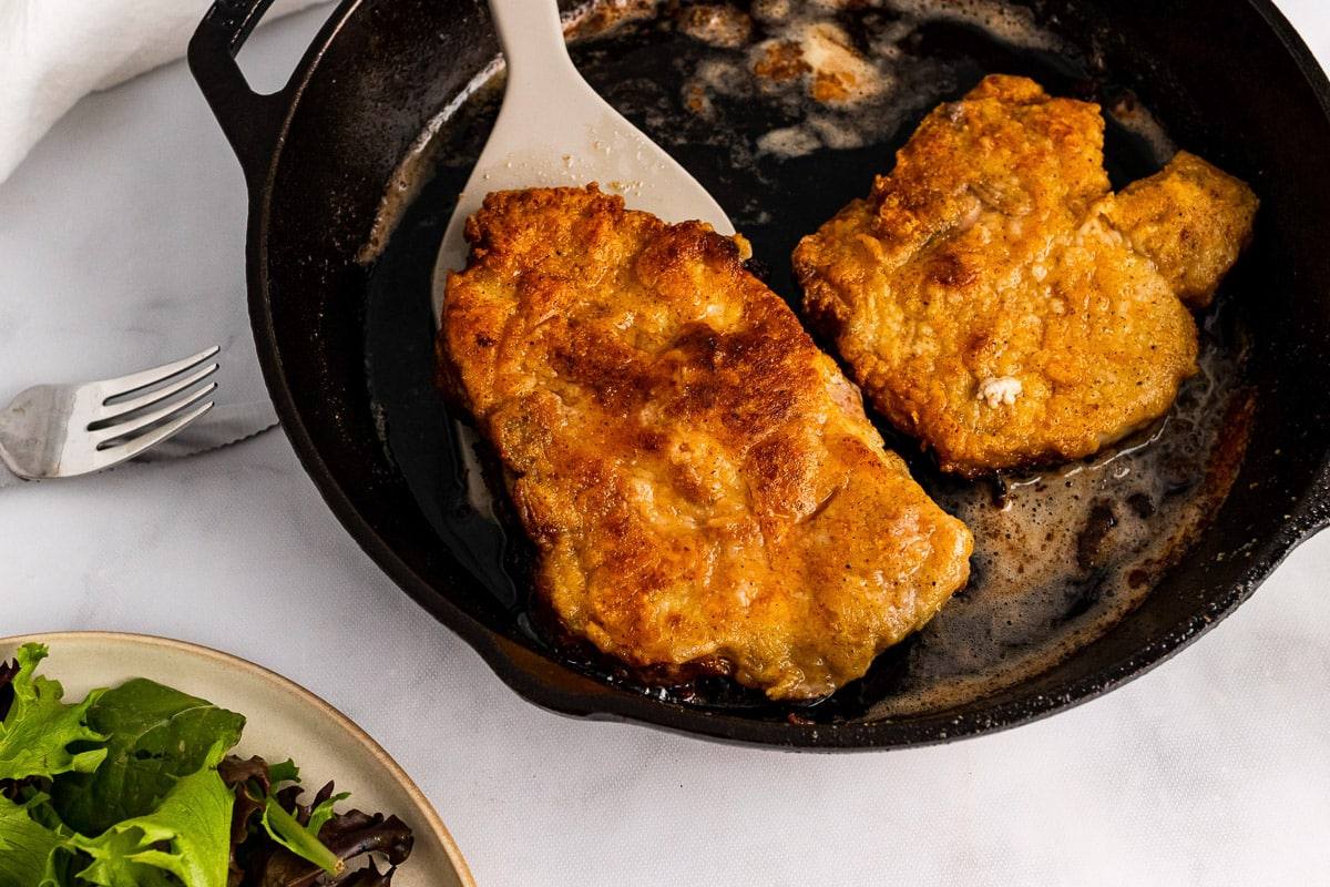 scooping one southern fried pork chop out of the skillet