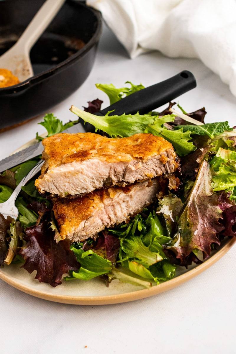pieces of cut southern fried pork chop on a lettuce-filled plate with knife and fork