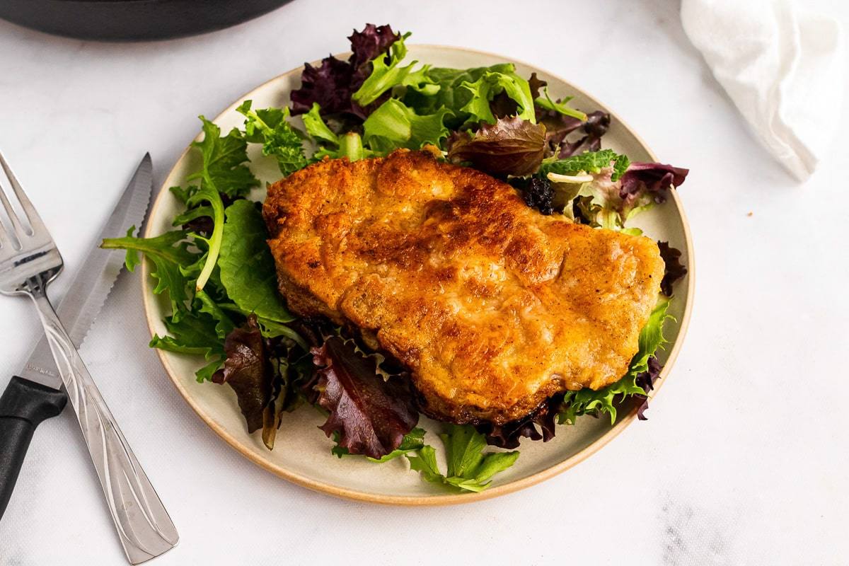 plate of southern fried pork chop and lettuce next to crossed fork and knife
