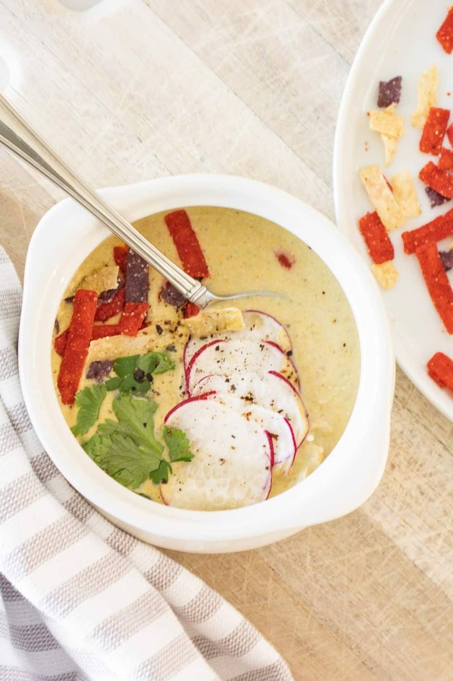 Bowl of spicy creamy chicken poblano soup topped with sliced radishes, tortilla strips and cilantro