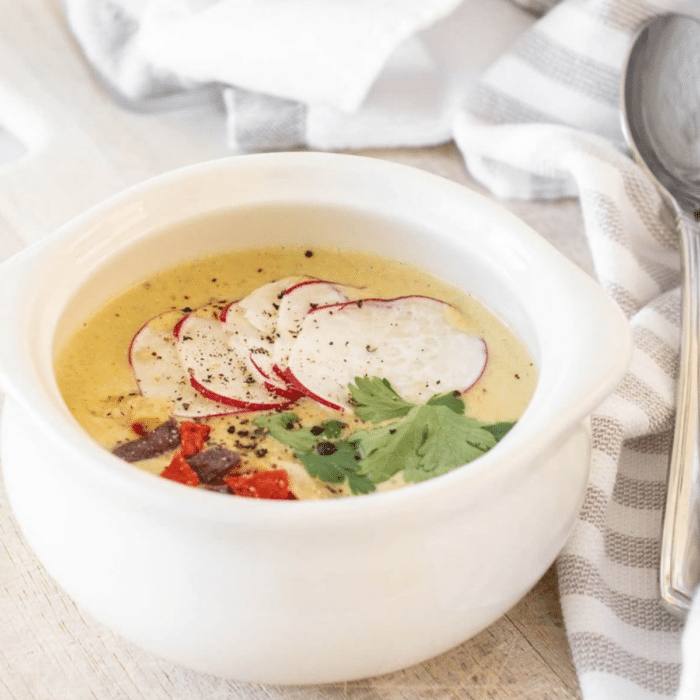 Spicy creamy chicken poblano soup in a white bowl topped with sliced radishes, tortilla strips and cilantro