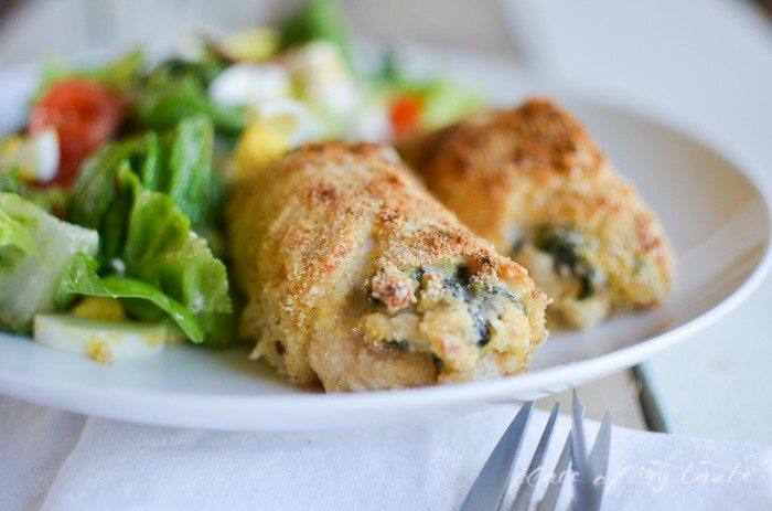 Two golden bread crumb coated spinach and feta stuffed chicken breasts on a white plate with a green salad