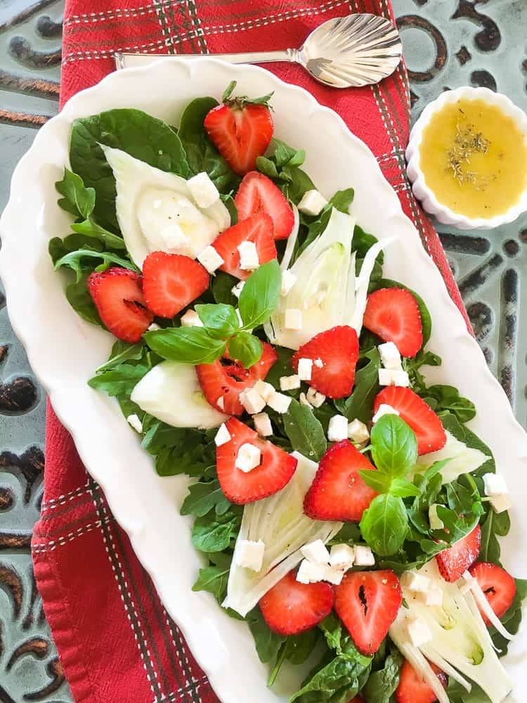 top down view of strawberry fennel salad served on a white oval platter with a cup of homemade dressing on the side
