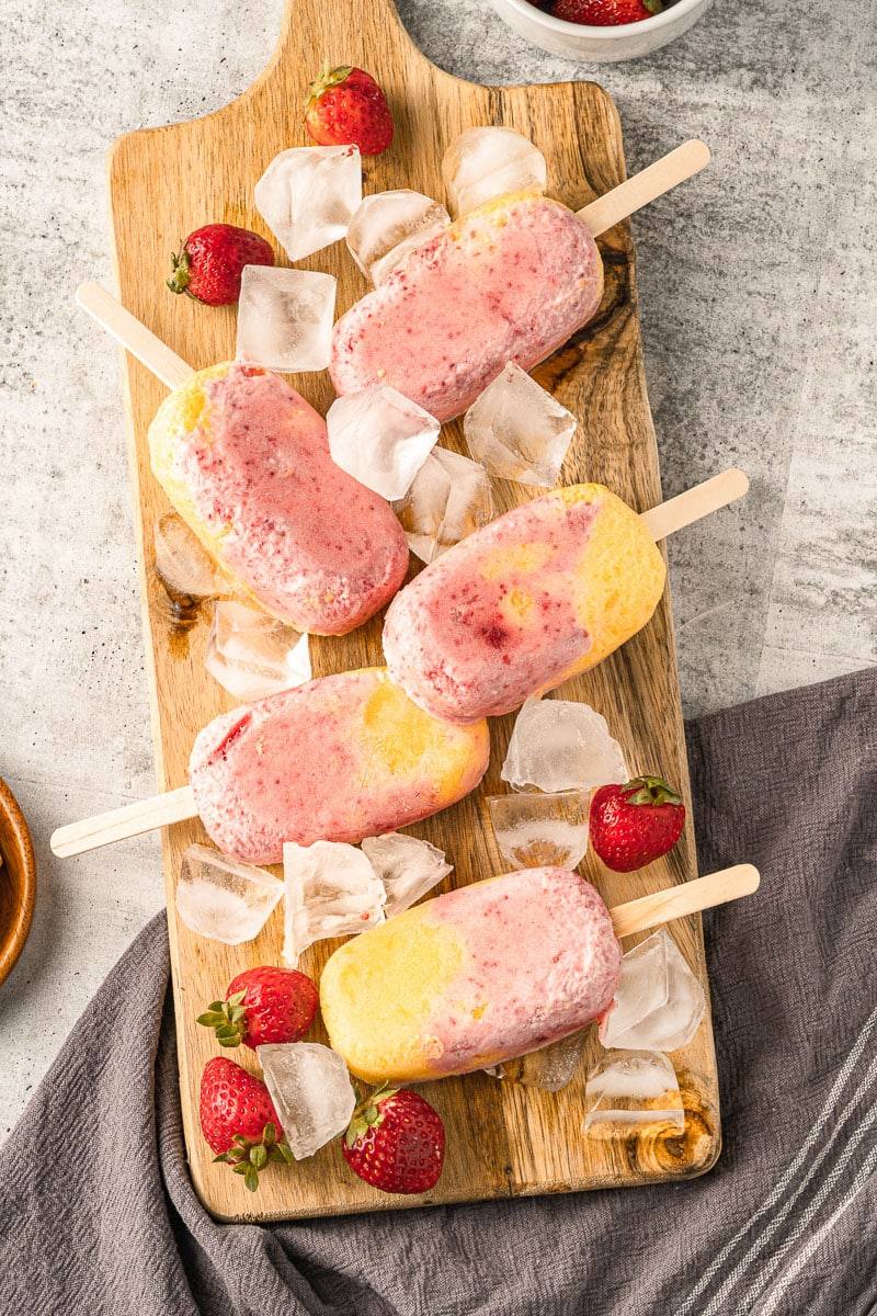 strawberry mango popsicles on a wooden platter