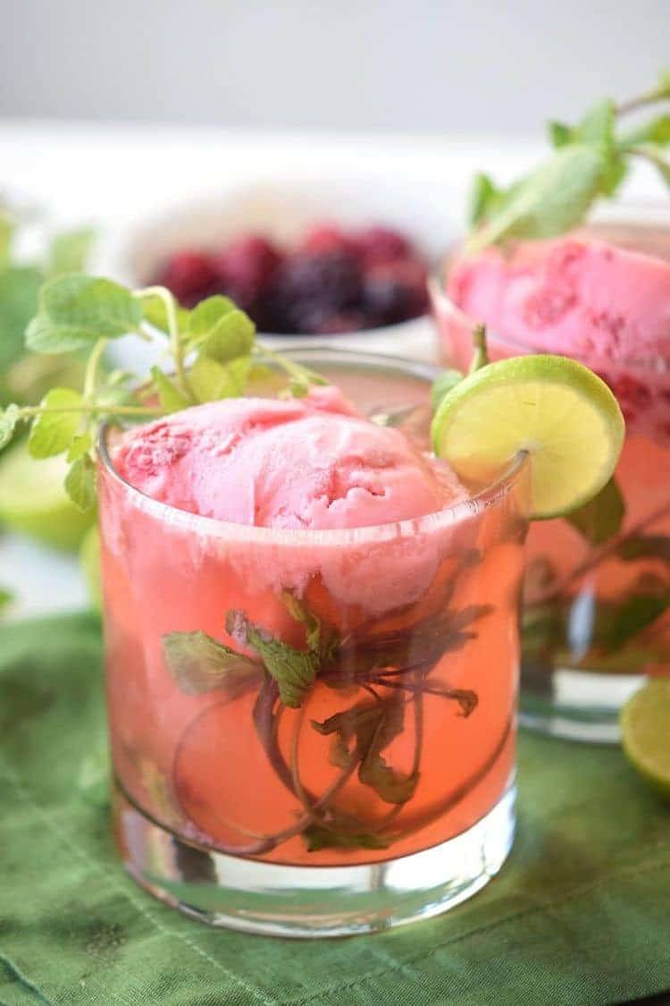 strawberry mojito float being served garnished wint lime wedges and mint sprigs