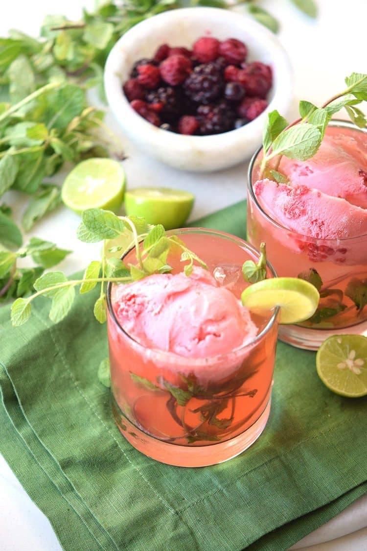 strawberry mojito with a scoop of ice cream being served garnished wint lime wedges and mint sprigs
