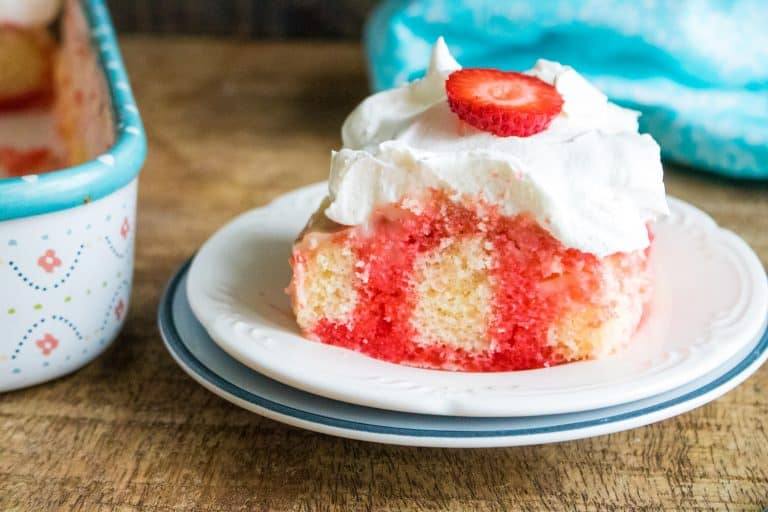 close-up of one slice of strawberry poke cake served on white plate next to a blue cloth napkin