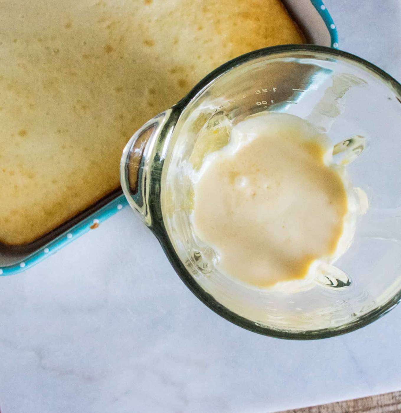 top-down view of baked white sheet cake with holes poked in top and clear glass bender pitcher filled with peach cream mixture