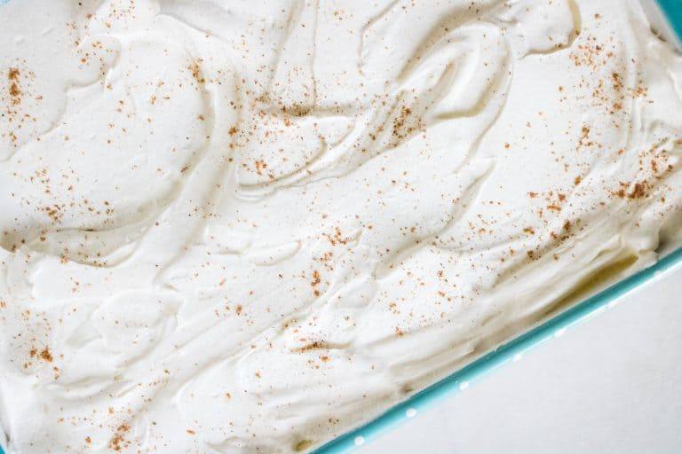 top-down view of the completed Summer Peach Pie Poke Cake in baking dish with a sprinkling of nutmeg on top of the whipped topping frosting