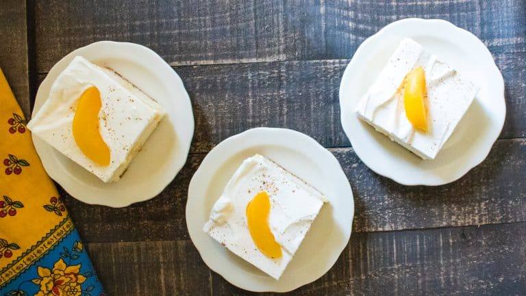 top-down view of three slices of Summer Peach Pie Poke Cake served on white plates with scalloped edges