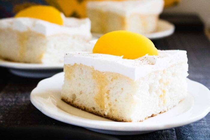 Two slices of Summer Peach Poke Cake served on white dessert plates