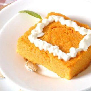 Square of low-fat crustless pumpkin pie with whipped topping on a white plate with pumpkin seeds