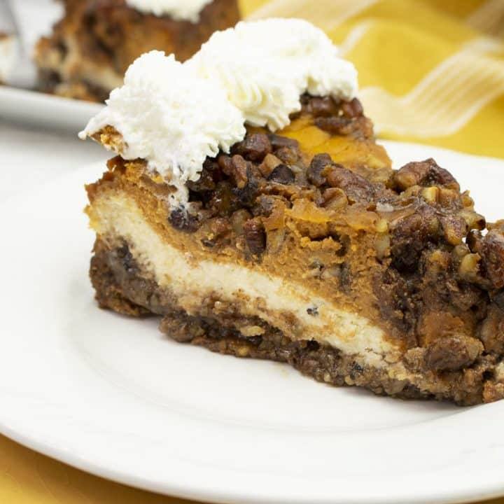 Slice of double layer pumpkin cheesecake with pecan crust and whipped cream on a white plate